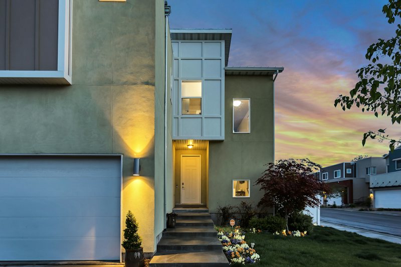 Modern two-story house with a lit front doorway under an evening sky