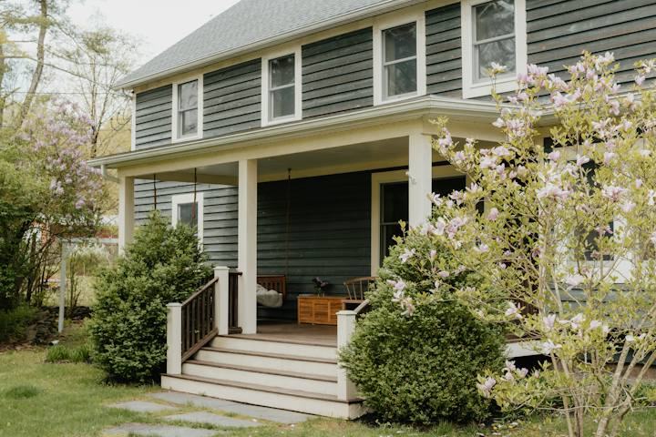 Gray house with a front porch and steps beside a flowering tree